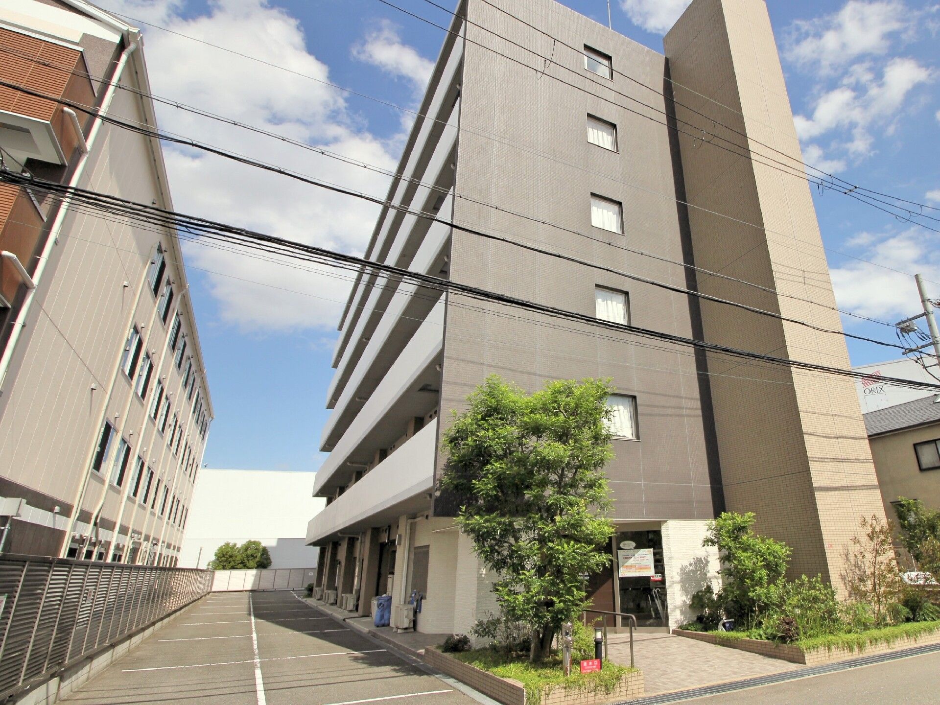外観とエントランスの様子。道路とエントランスの間には植物が植えられている。建物の横は駐車場になっている。