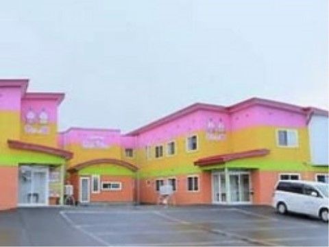 ピンク・黄色・黄緑・オレンジ色のボーダーの外壁。屋根は赤色でカラフル。