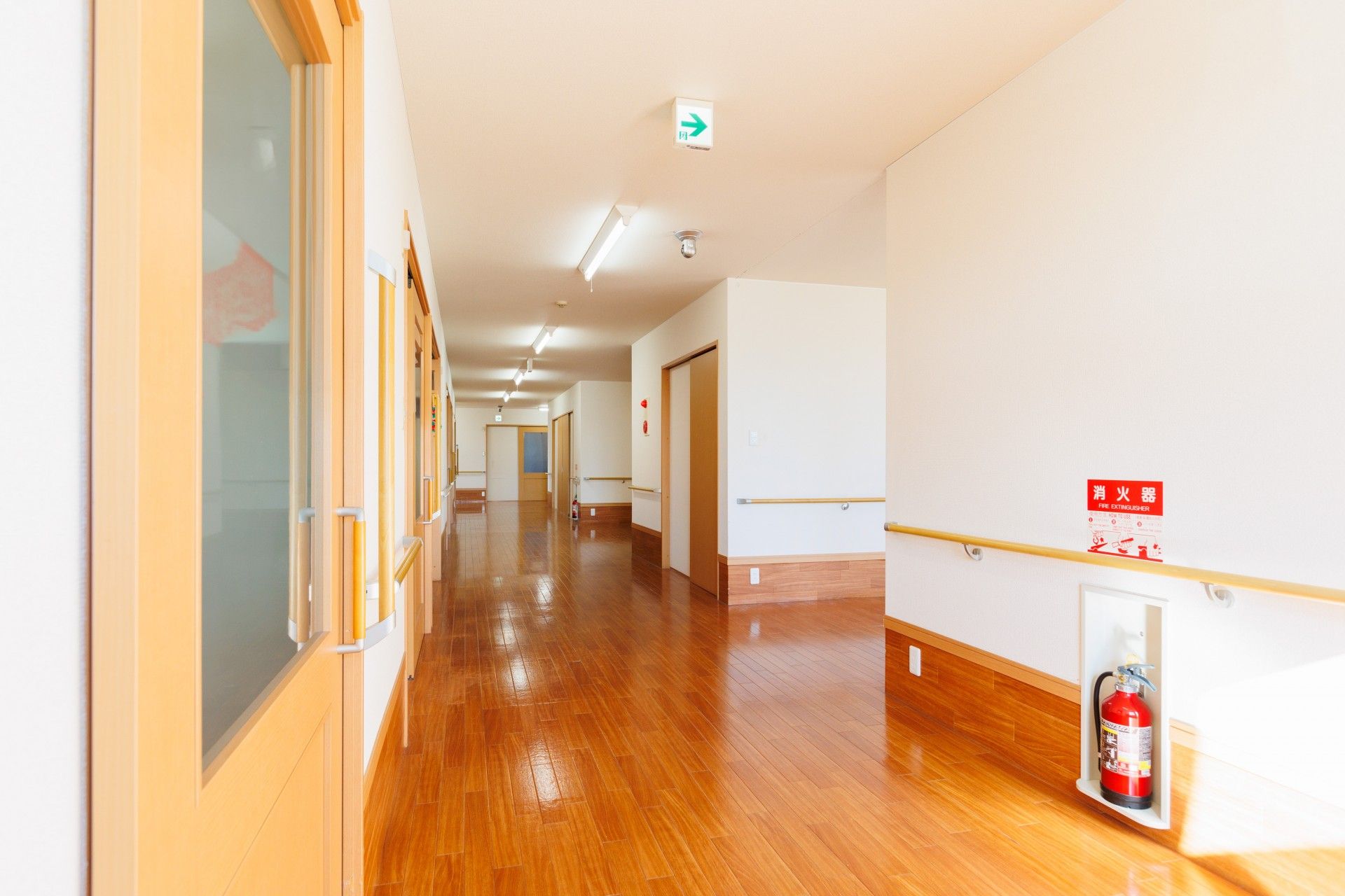 通路の幅が広く、つきあたりの窓から光が差し込み明るい。消火器が置かれている。