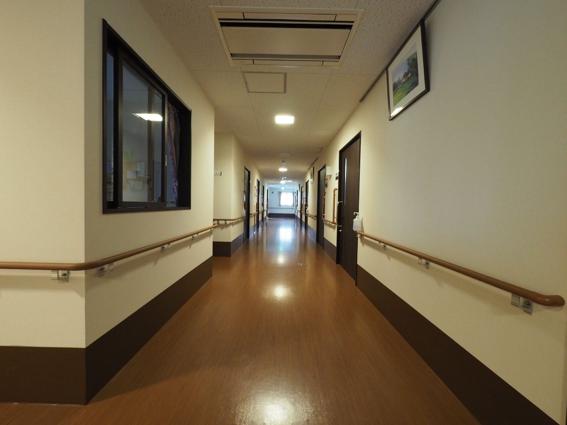 広々とした通路の廊下。床はフローリングのような木目調になっている。全面的に手すりがついていて、壁には絵が飾られている。