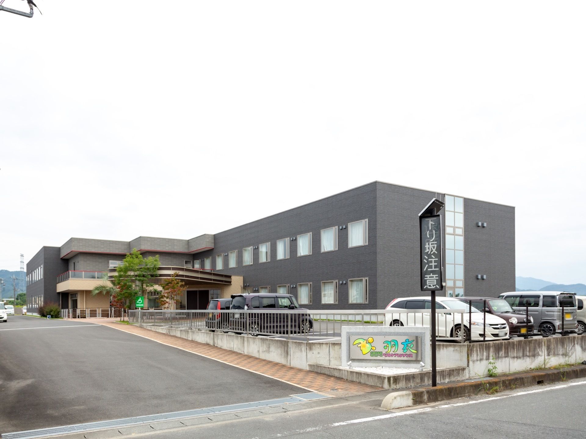 道路から施設の敷地内へは緩やかな勾配となっている。敷地の入り口に施設名の書かれた看板が掲げられている。