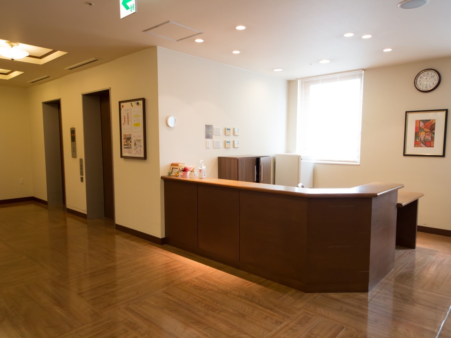 木目調の受付カウンターが設置されていて、カウンターの上には消毒用のボトルが置かれている。壁に時計と絵画がかけられている。