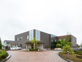 大きな２階建ての施設で、外壁には多数の窓を設けている。建物の前やアプローチの脇には、植栽が施されている。