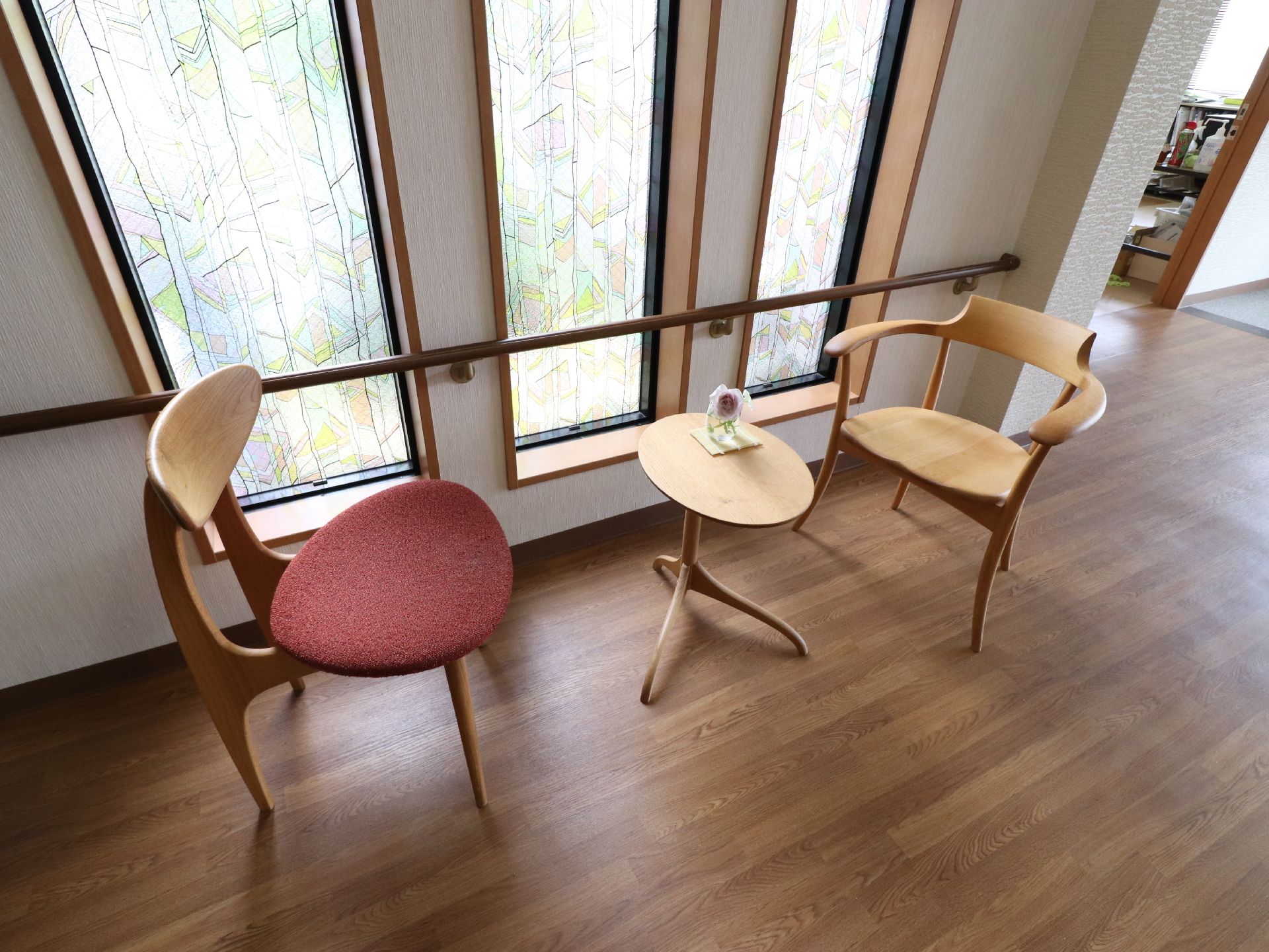通路に丸テーブルを一つ、いすを2脚おいてある。窓はステンドグラス風でおしゃれな雰囲気。また、窓側には手すりがついている。