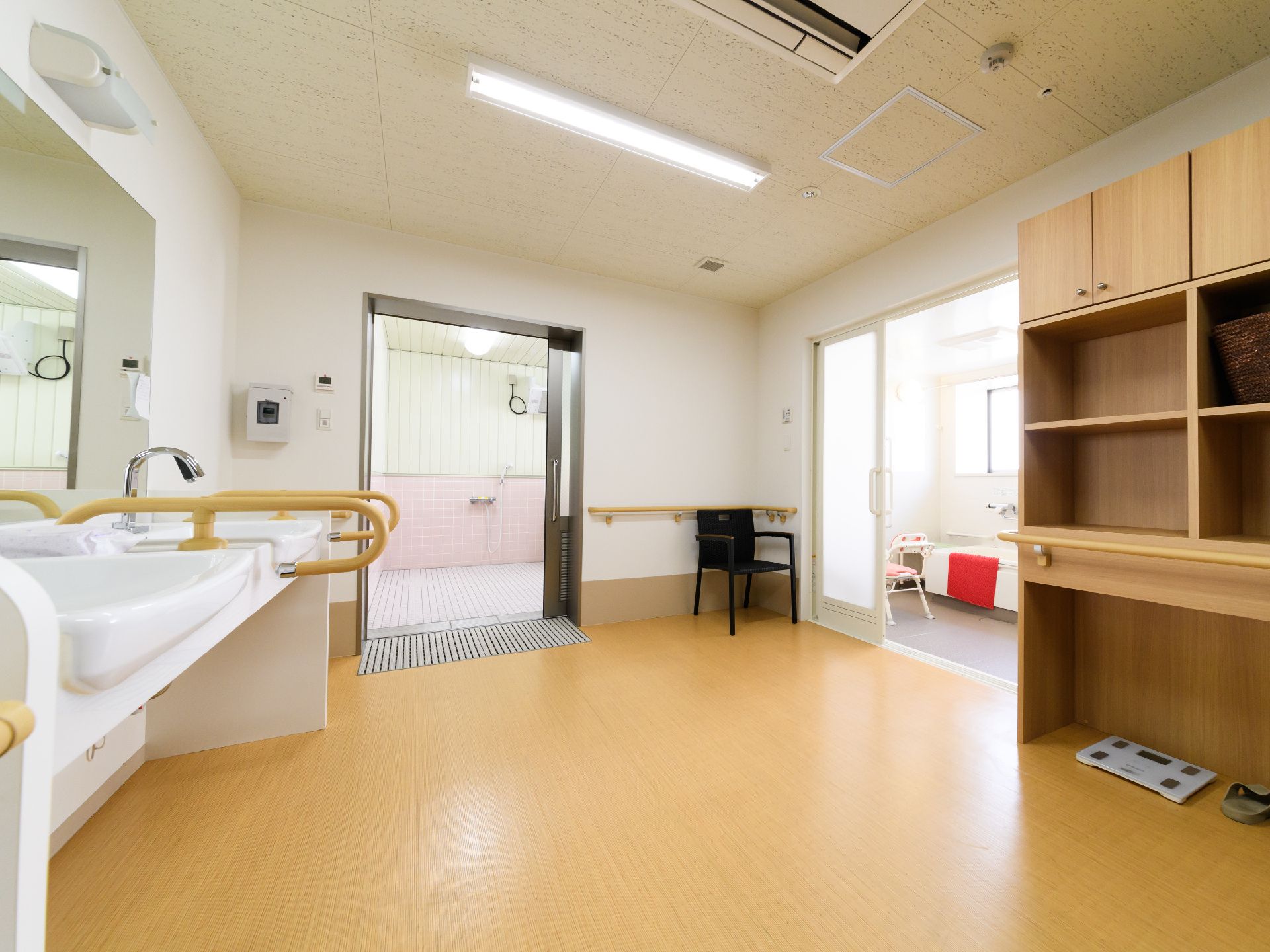 機械浴室と通常の浴室の脱衣所は同じ場所になっている。手すりや椅子が見受けられ、安全に気を配っている。