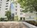 ６階建てのマンションとその後ろに８階建ての別の棟が建てられている。１階の施設前には駐車スペースがある。