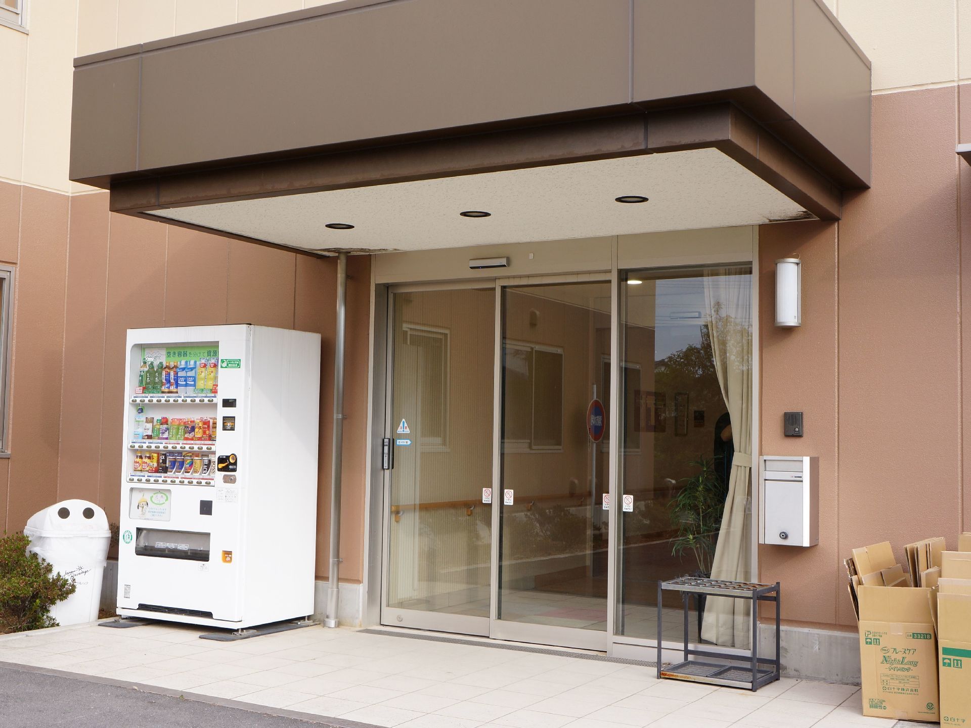 建物の入り口は自動ドアである。ドアの外左側に、自動販売機が設置されている。反対側には、郵便受けや傘立てがある。