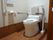 出入り口が引き戸のトイレで、壁には温水洗浄便座のリモコンや、緊急用の呼び出しボタン、手すりが設置されている。