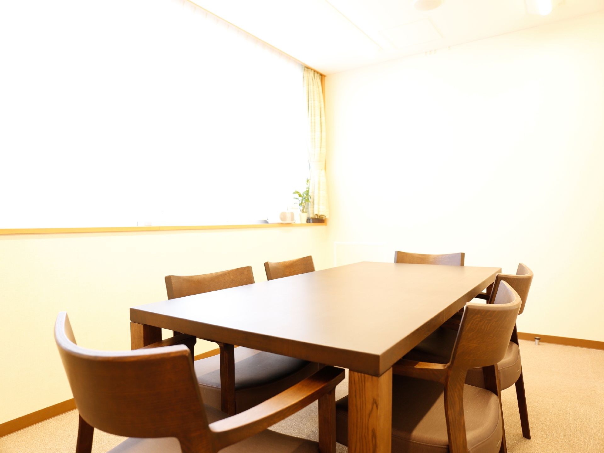 木目調のテーブルと6脚の椅子が中央に並んでいる。白い部屋に大きな窓から外の明かりがたっぷりと差し込んでいる。