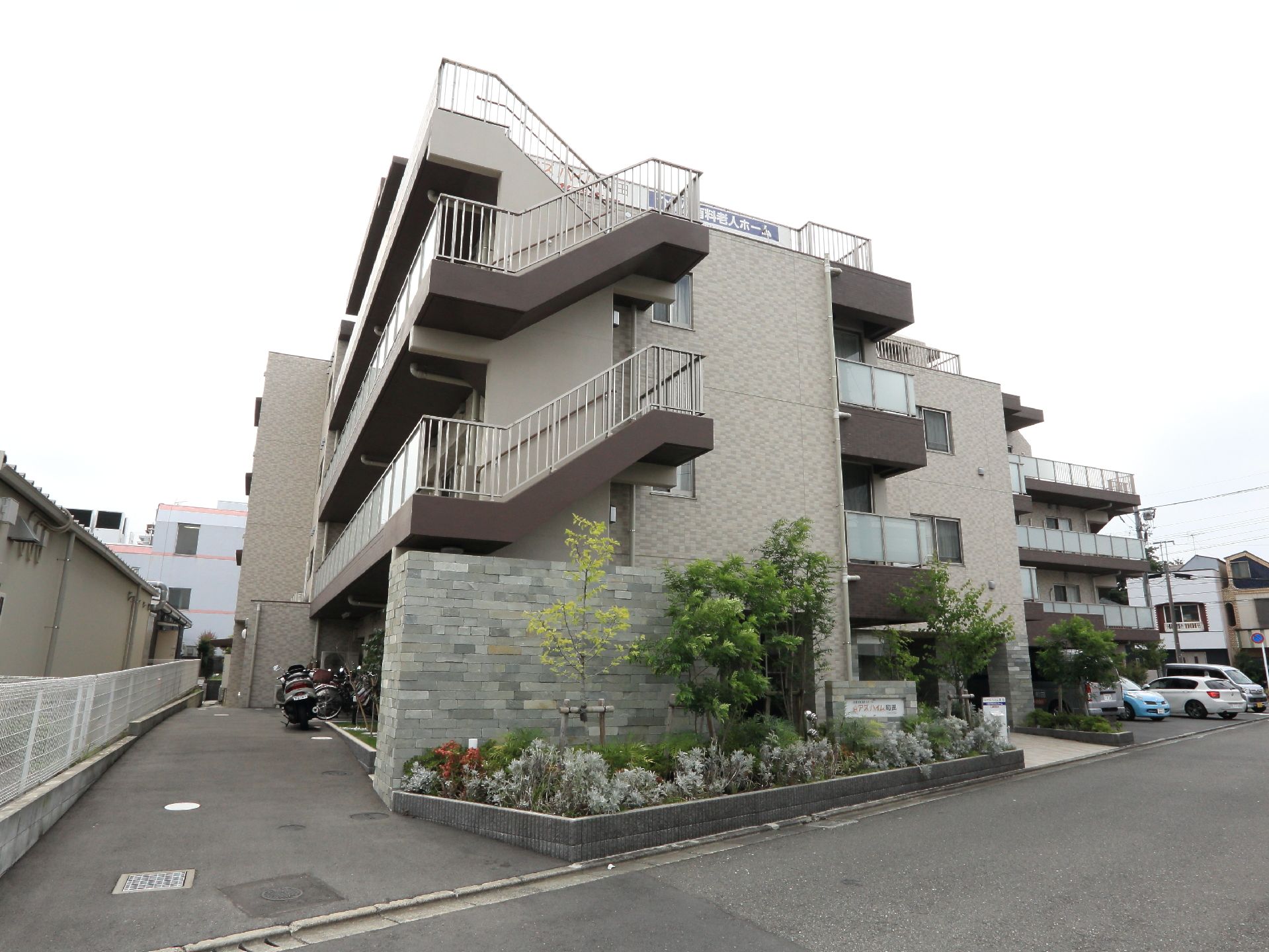 鉄筋コンクリート造りで、地上4階建ての強固な作りの建物。裏手にある駐輪所と正面にある駐車場も見える。