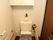 トイレには手すりがしっかりと設置されている。上部には棚が作り付けられている。タンクの上には花が飾られている。