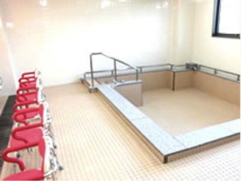 白とベージュで施された、明るい雰囲気の浴室である。洗い場に、赤色の介護用シャワーチェアが備え付けられている。