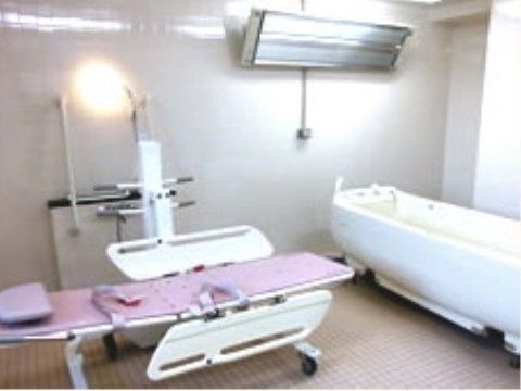 浴室にピンク色の担架、ホワイトの介護浴槽が備え付けられている。寝た姿勢での入浴が可能な介護専用機器である。