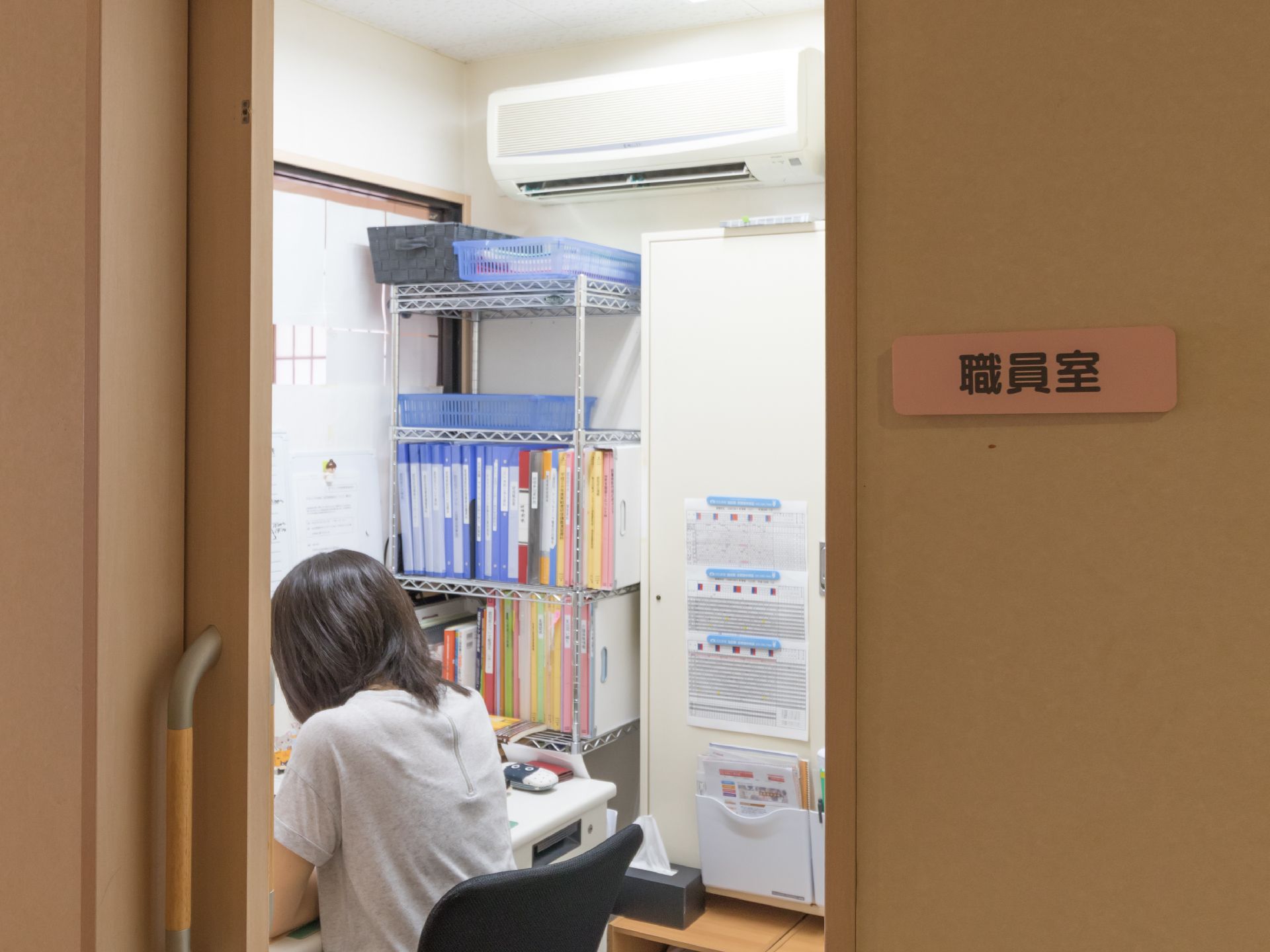 職員室があり、部屋の中には机と椅子、ファイルの置かれたラックがある。ドアは横開きになっており、開けやすい工夫がされている。