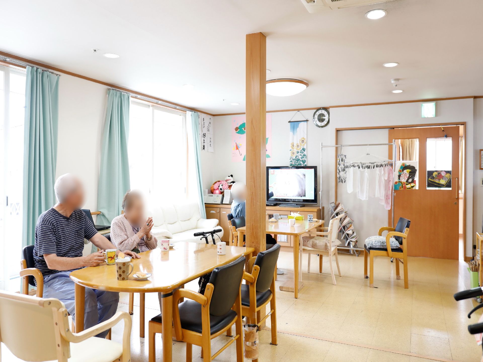 お茶の時間の様子。利用者の人たちが集まっている。お菓子とお茶が用意されており、テレビを見ている人もいる。