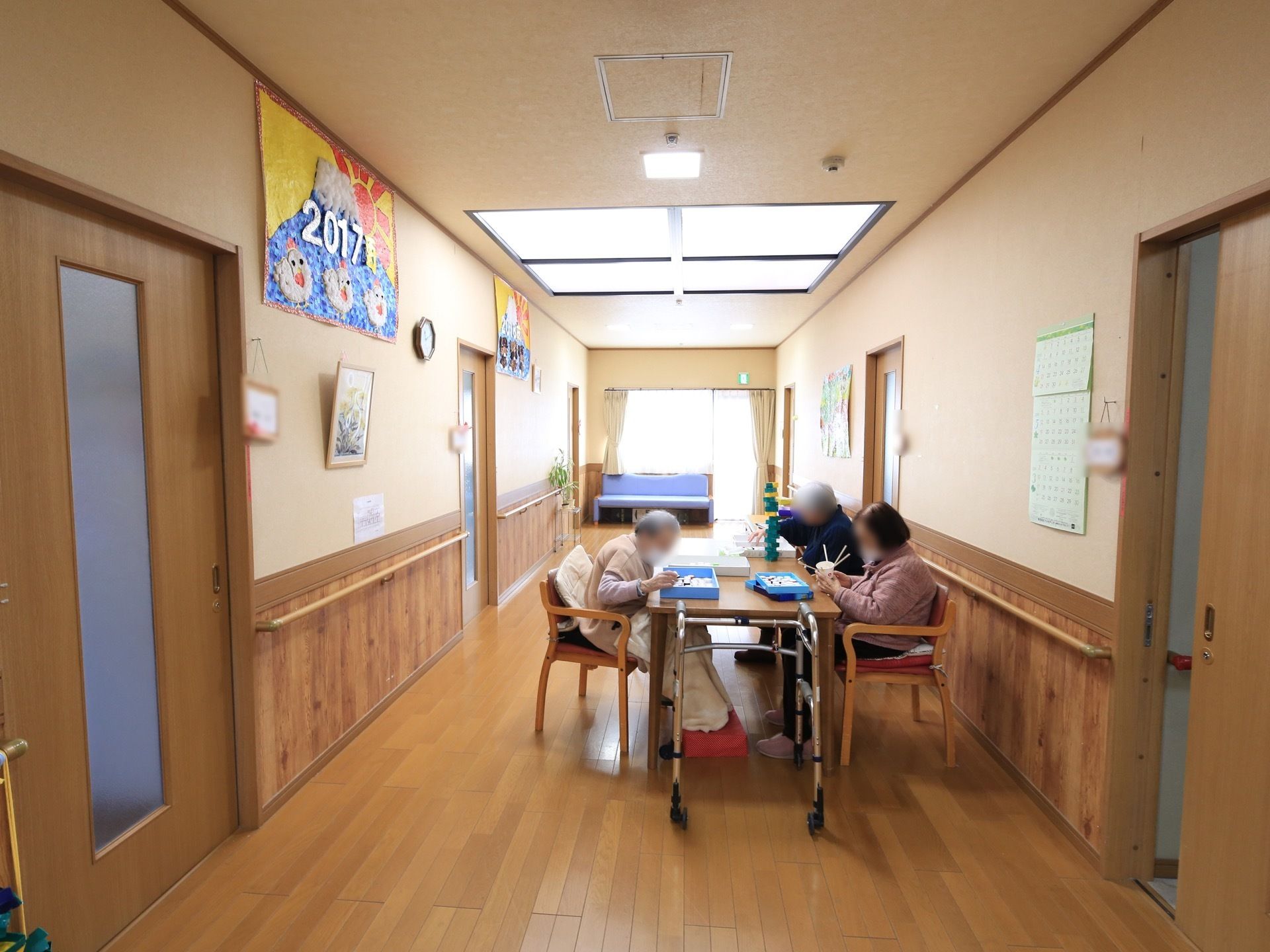 居室前の廊下にテーブルセットが設置され、女性の入居者様3名がテーブルに着き、それぞれに作品を作られている。