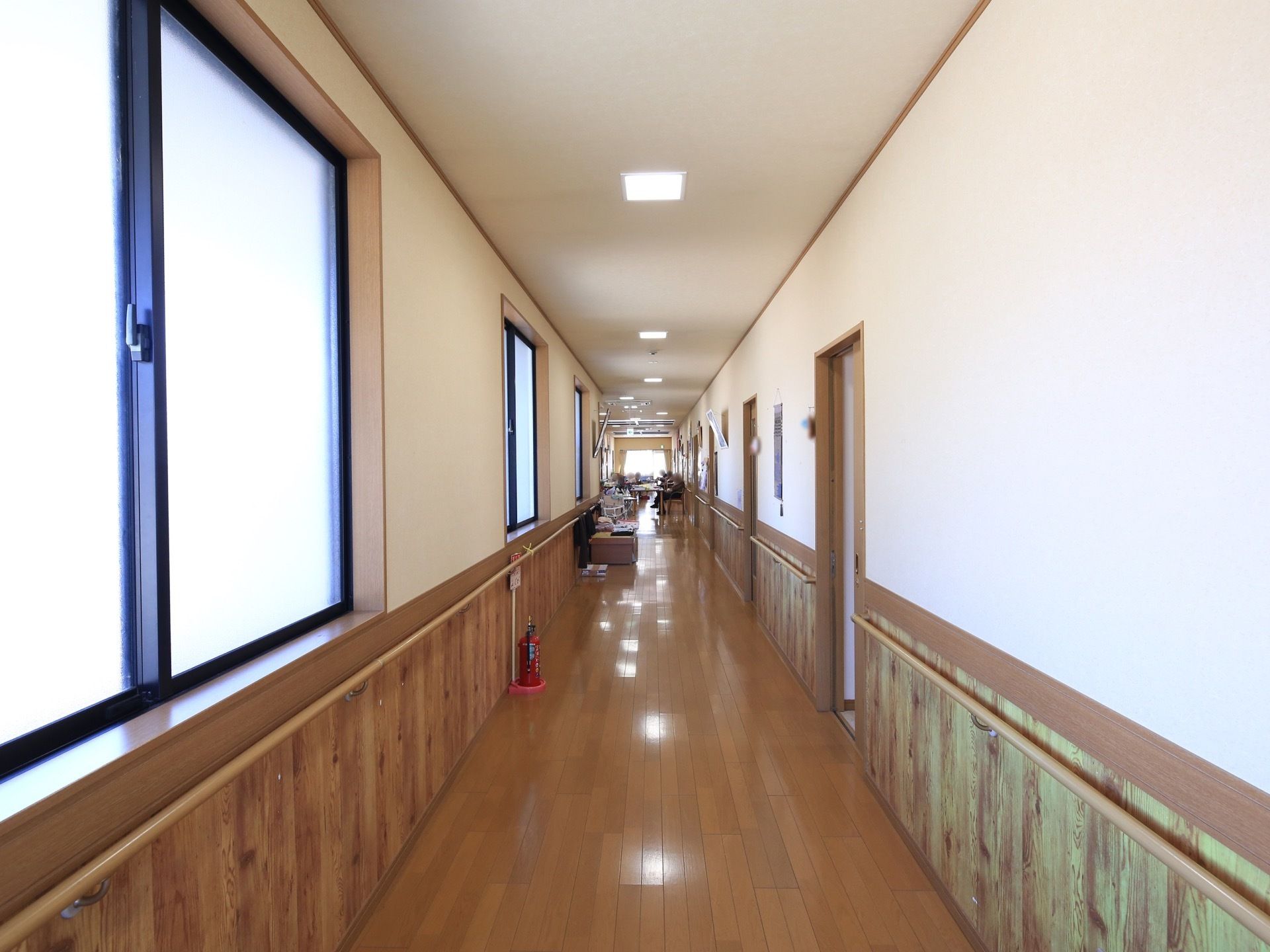 木目調を基調にした廊下には窓が設置されている。両サイドの壁には手すりが取り付けられ、消火器が置かれている。