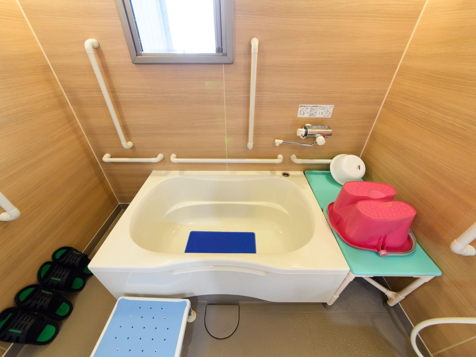 木目調の壁に囲まれて、備えている白色の浴槽である。小さな窓があり、壁際には、手すりを縦横に設置している。