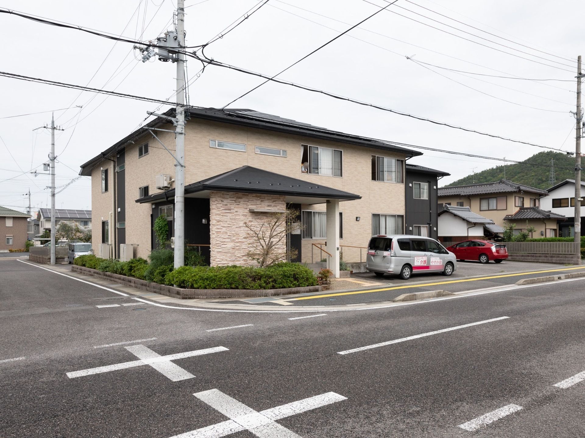 2階の窓から入居者様が顔を出している。屋根付きの玄関となっており、柱にインターホンが設置されている。