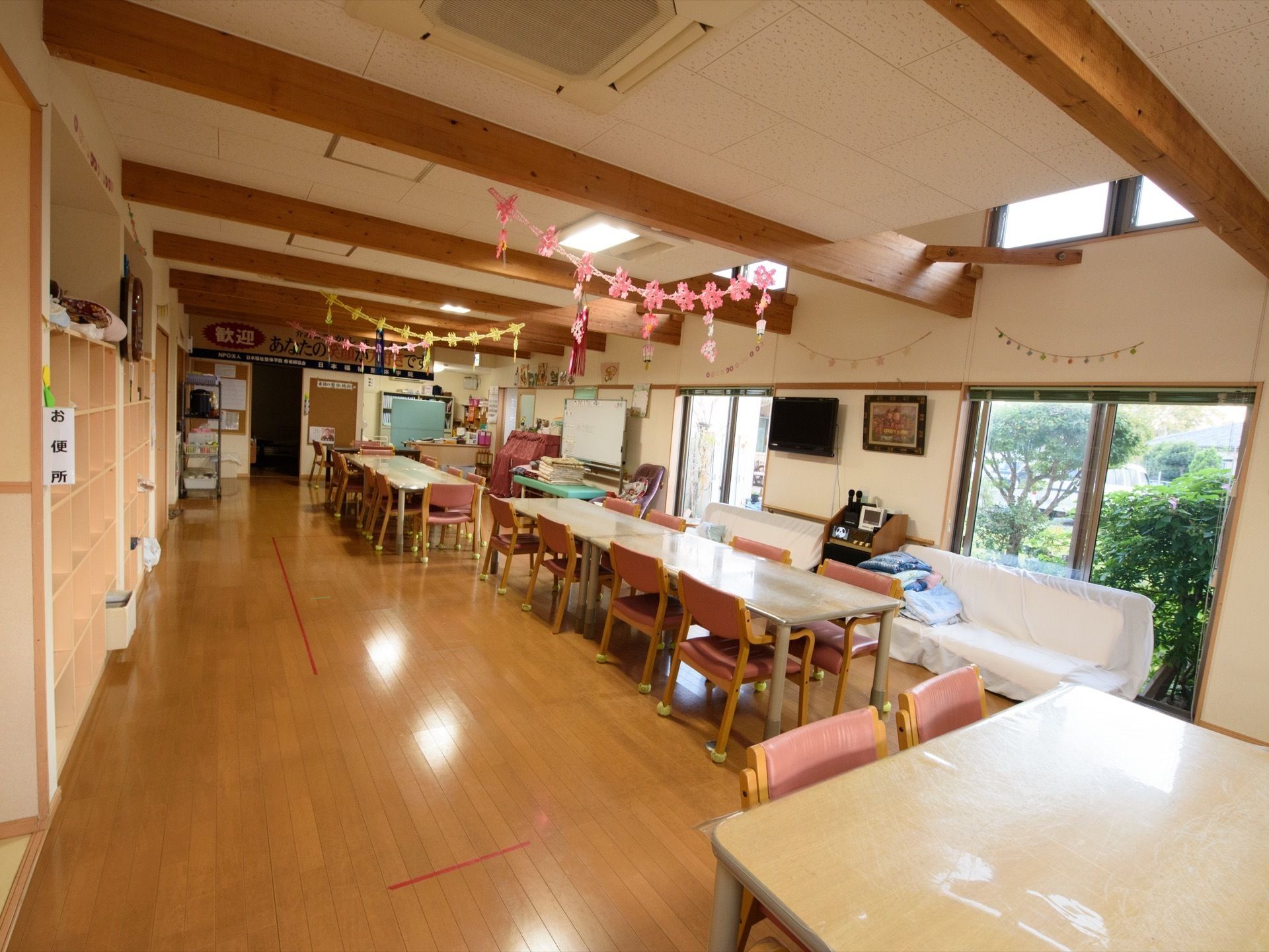 奥行きがあり広々とした共有スペース。窓からは青々とした緑が見える。天井からは手作りの飾りがあり、窓側にはソファーを置いている。
