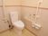 洋式トイレの両側に、手すりが取り付けられている。右側の壁に、トイレのスイッチとナースコールが設置されている。