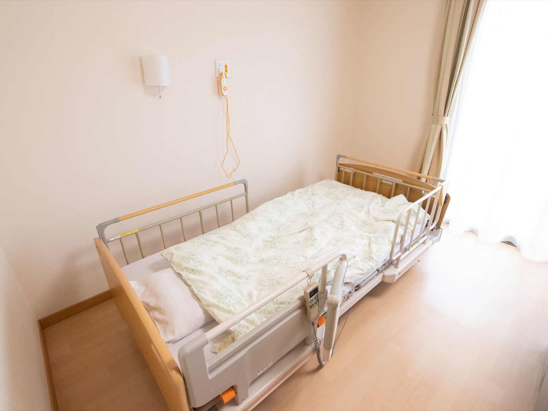 リモコンと転落防止のフェンスが取りつけられた電動の介護ベッドが用意されている。上には白い清潔感のある布団が敷かれている。