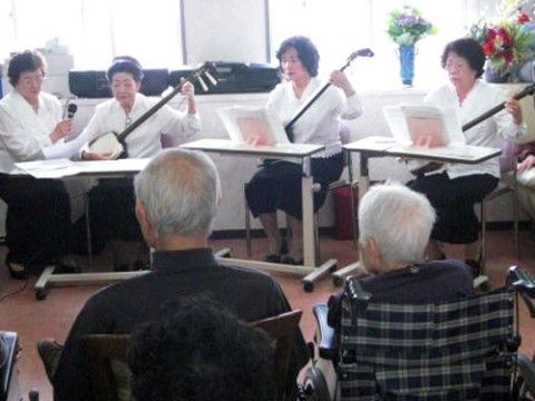 三味線を披露している女性たちを、椅子に座って見ている入居者たち