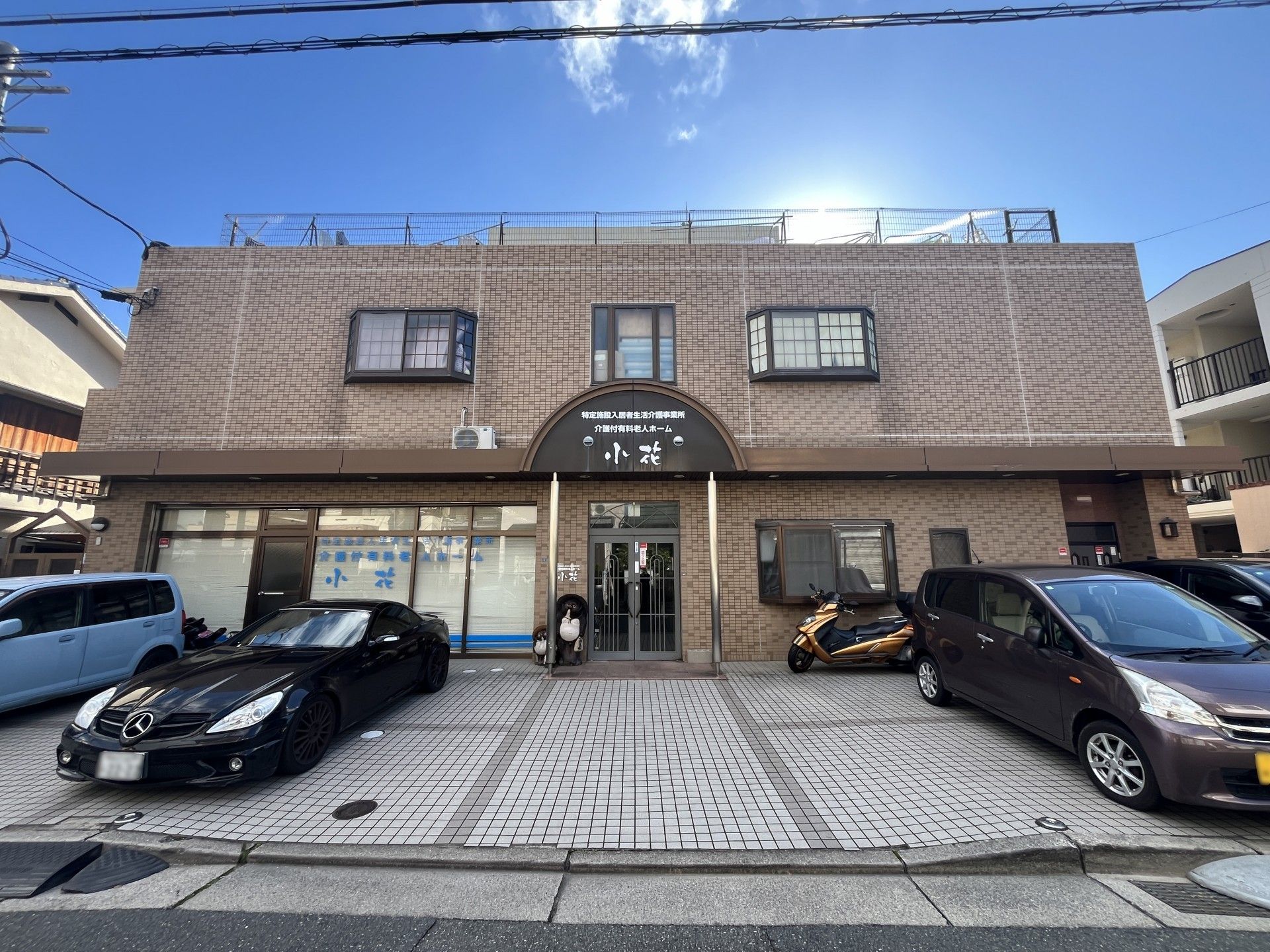 建物前に駐車スペースを備えた、2階建てのブラウン色の施設外観