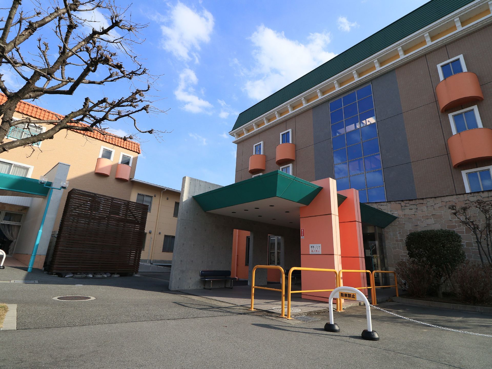茶色やオレンジ、深緑、大きなガラス窓などを使用した、色合いの鮮やかな外観である。玄関前に車止めが立てられている。