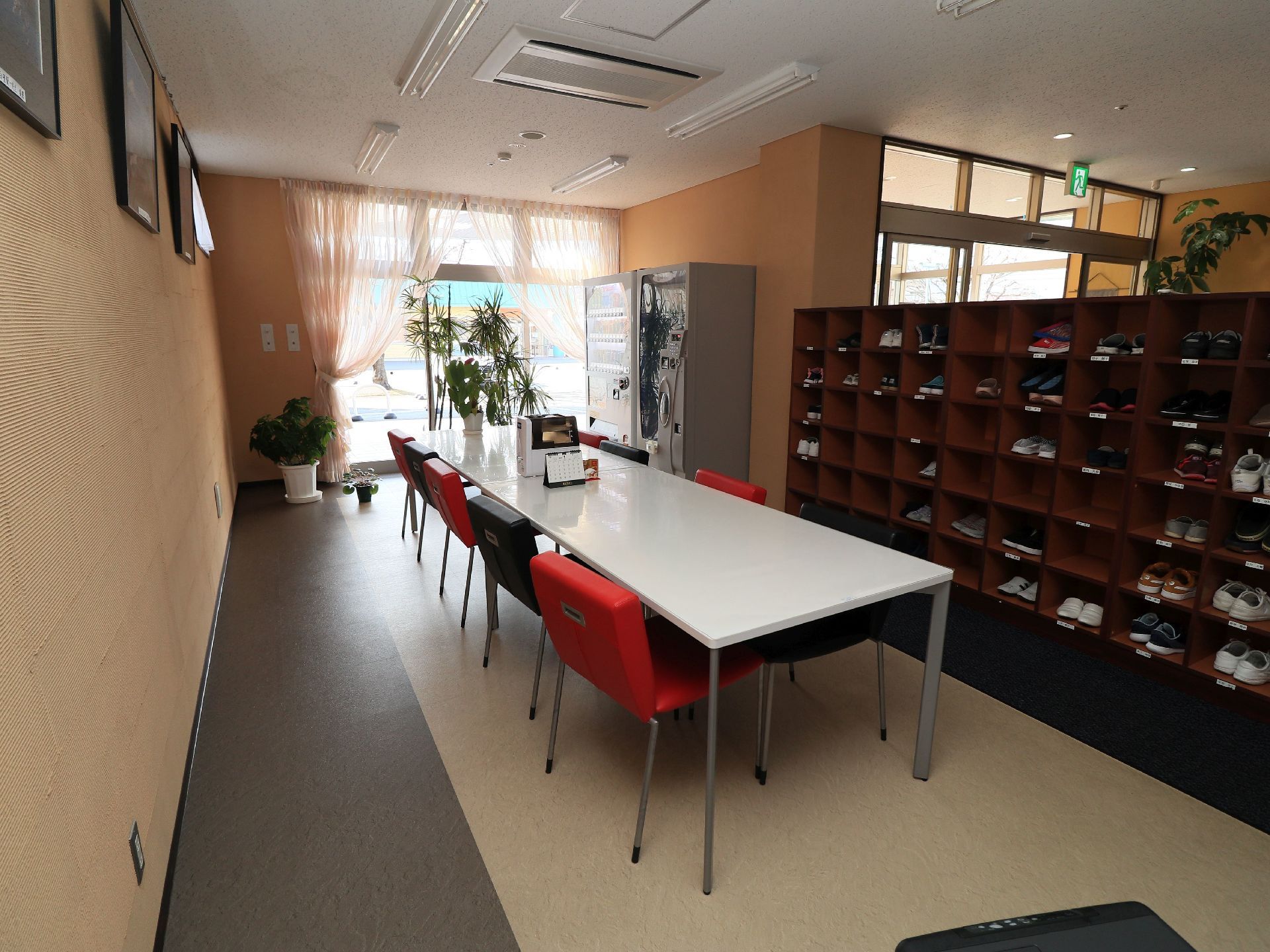 玄関内部には、個人用の靴入れが設置されている。白色の天板のテーブルとカラフルな椅子が置かれたスペースもある。