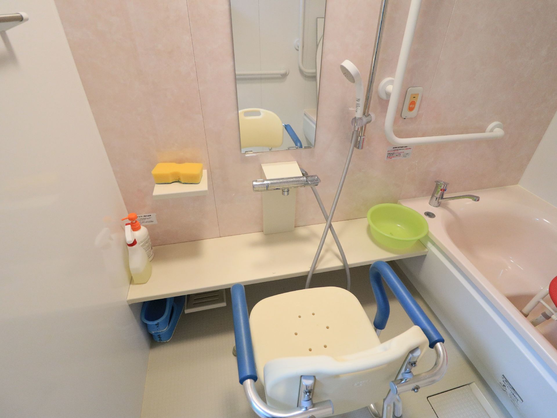 浴室に、背もたれやひじ掛けがついた椅子が置かれている。浴槽に入る所に縦横の大きな手すりがあり、その近くにナースコールボタンがついている。