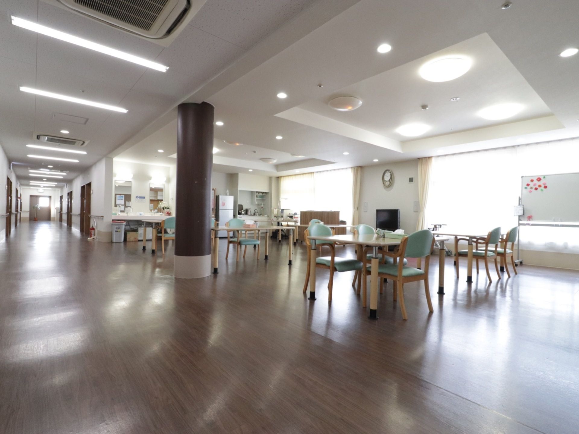廊下からつながる多目的ホール。広さのある空間に複数台テーブルが置かれている。大きな窓が光を取り込んでいる。カウンターもある。