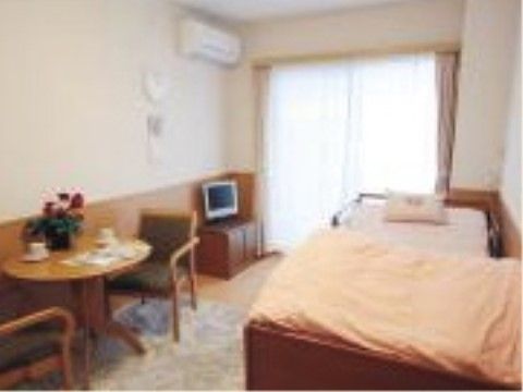 室内にはテレビやテレビ台、ベッド・丸テーブルセットが置かれており、腰壁と家具が木製なので温かみのある部屋になっている。