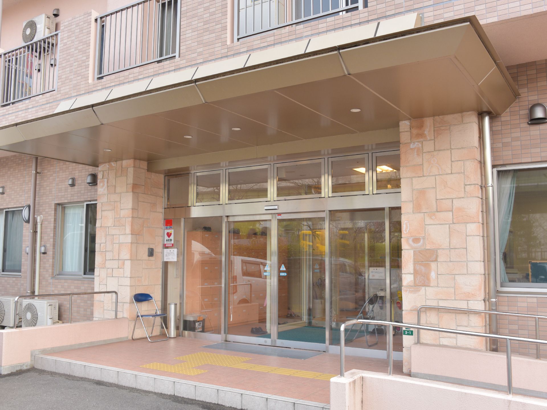 施設の入り口には1段の段差と手すり付きのスロープがある。入り口の横には灰皿と椅子が1脚置かれている。入り口は自動ドア。