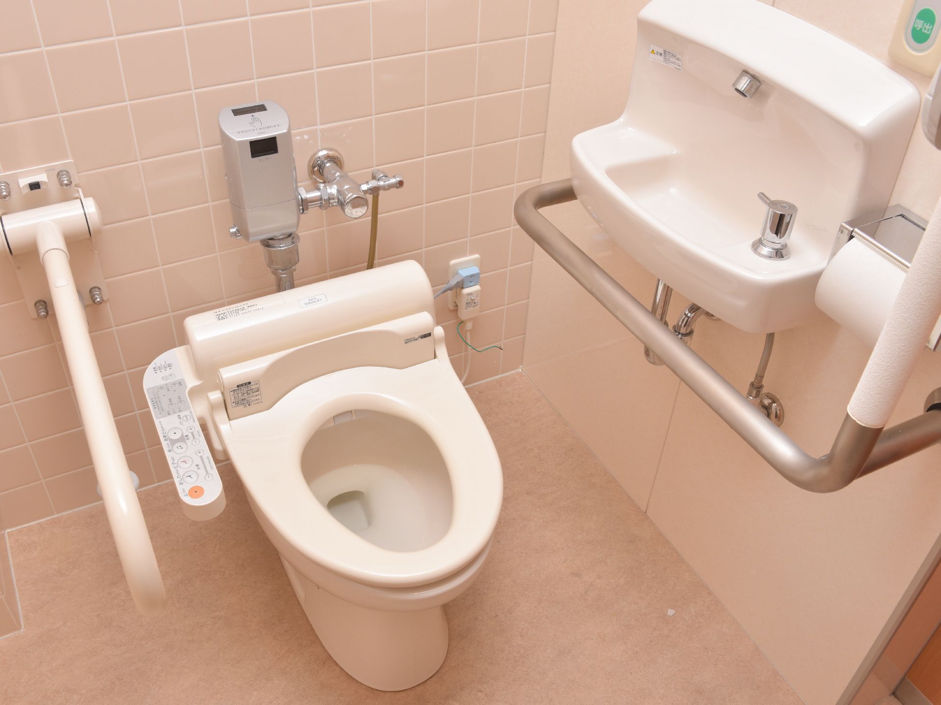 トイレに手すりと緊急ボタンが設置されている。便座のパネルで操作が可能。手洗い場が壁に設置されている。