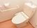 白色の壁に木目の床の内装のトイレである。壁にはエル型の手すりとトイレットペーパーホルダーが設置してある。