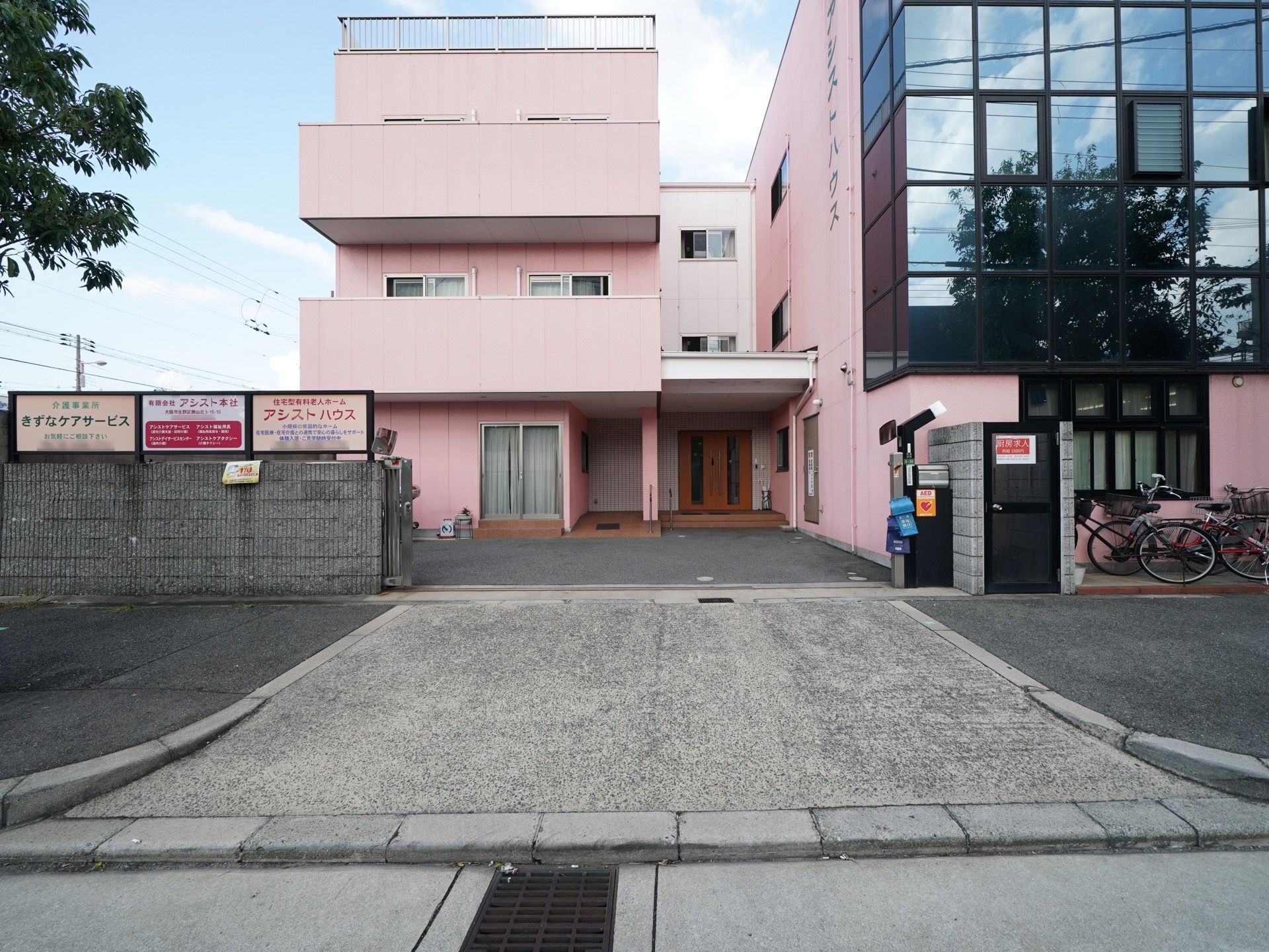 施設前の通りから玄関までは緩い上り坂で段差が無い。ピンク色の建物の前には、広い駐車スペースが設けられている。