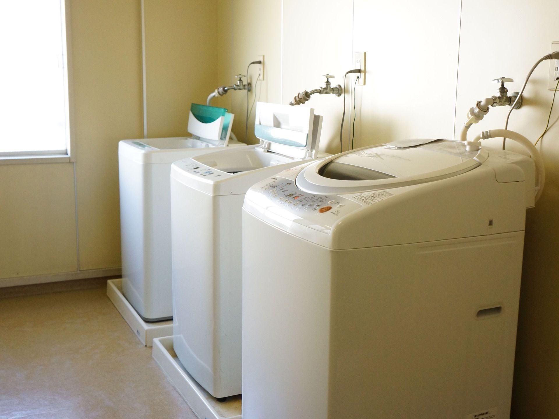 ランドリールームに３台の全自動洗濯機が完備されている。壁にそれぞれのコンセントと水道の蛇口がついている。
