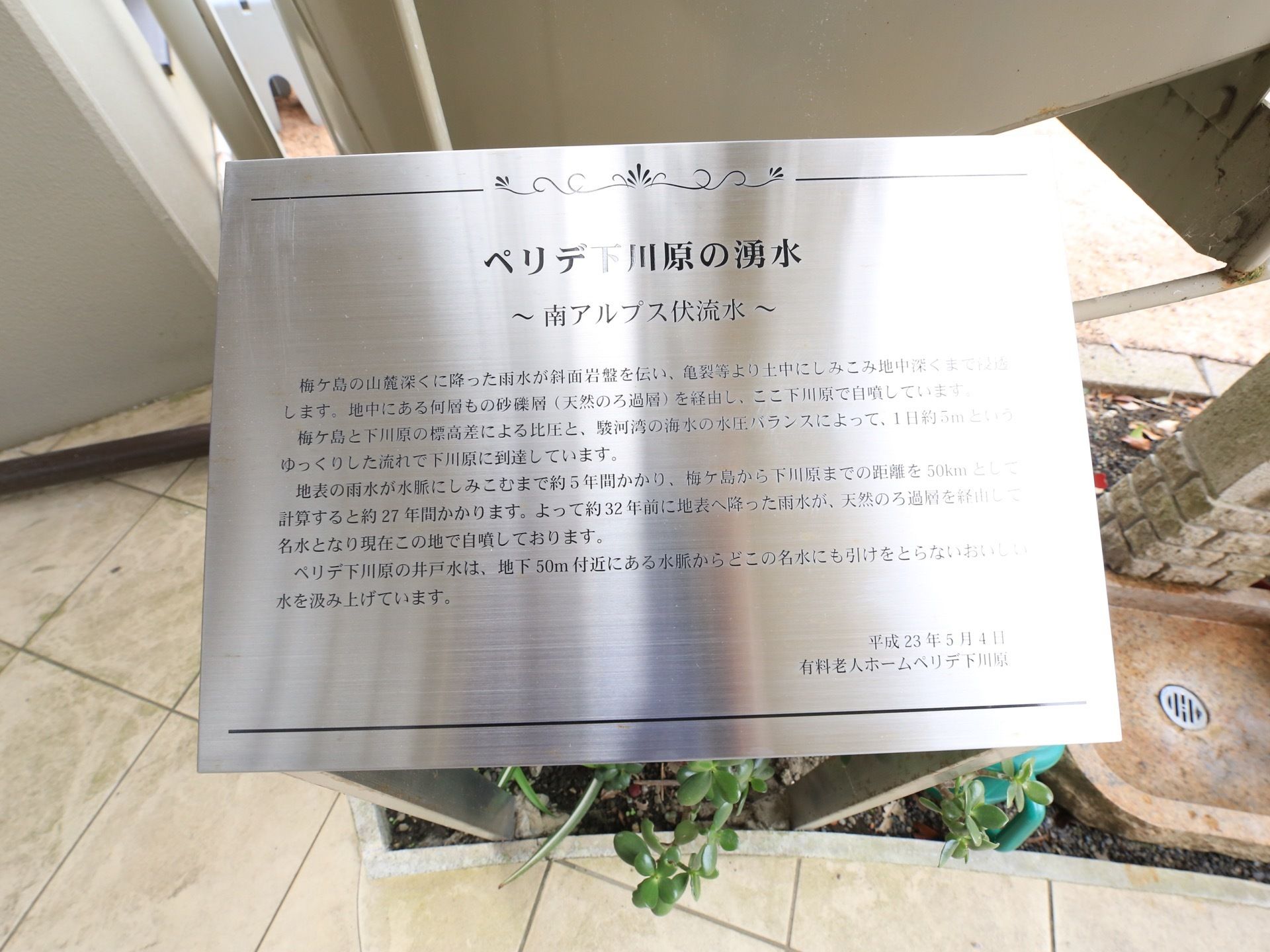 水栓の脇に看板が設置されている。南アルプスの伏流水が、この施設の敷地内で自噴していることを説明している。