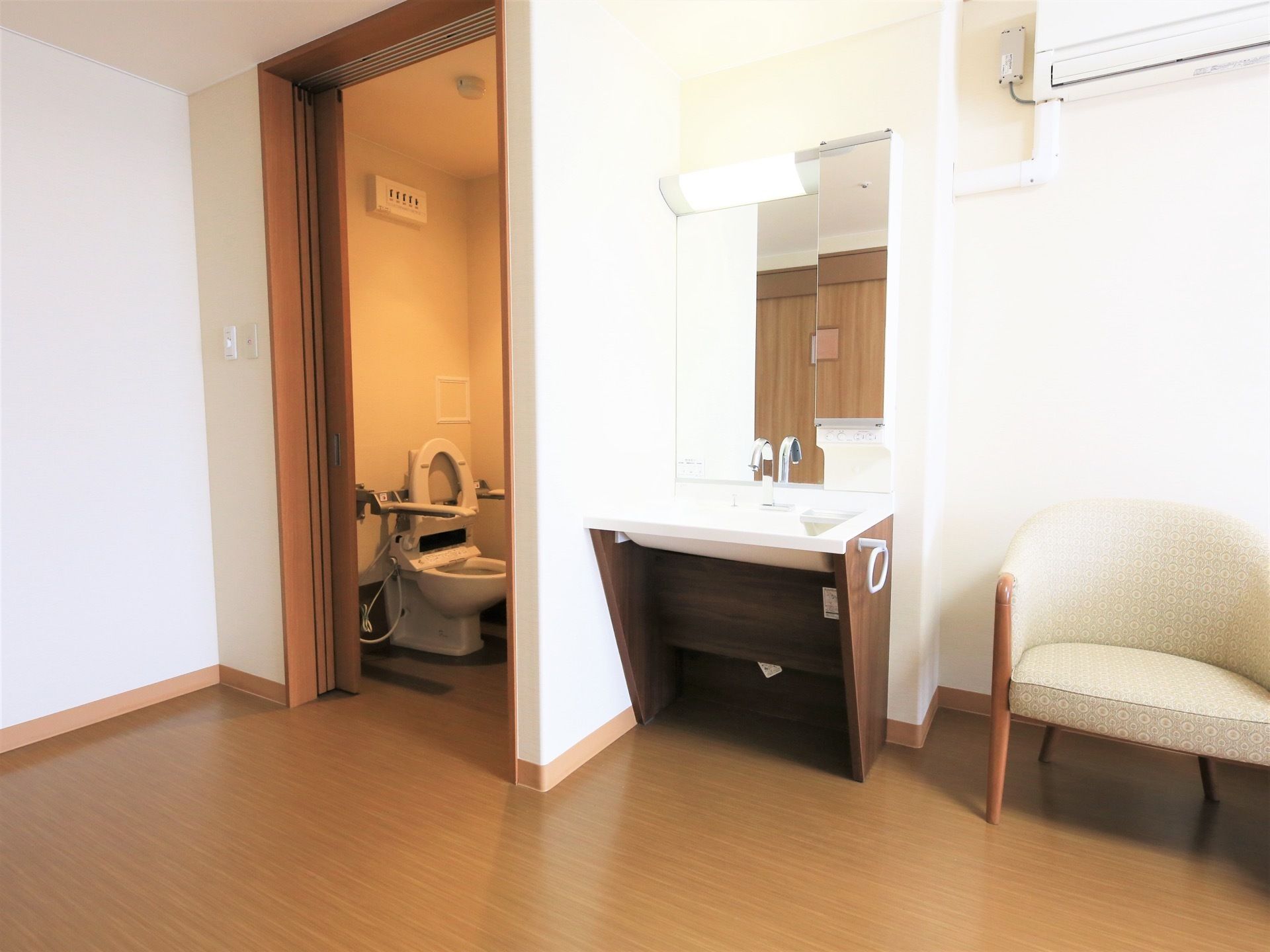 居室に、引き戸がついたトイレがある。便器の両脇に可動式の手すりが設置されている。室内には洗面台も用意されている。