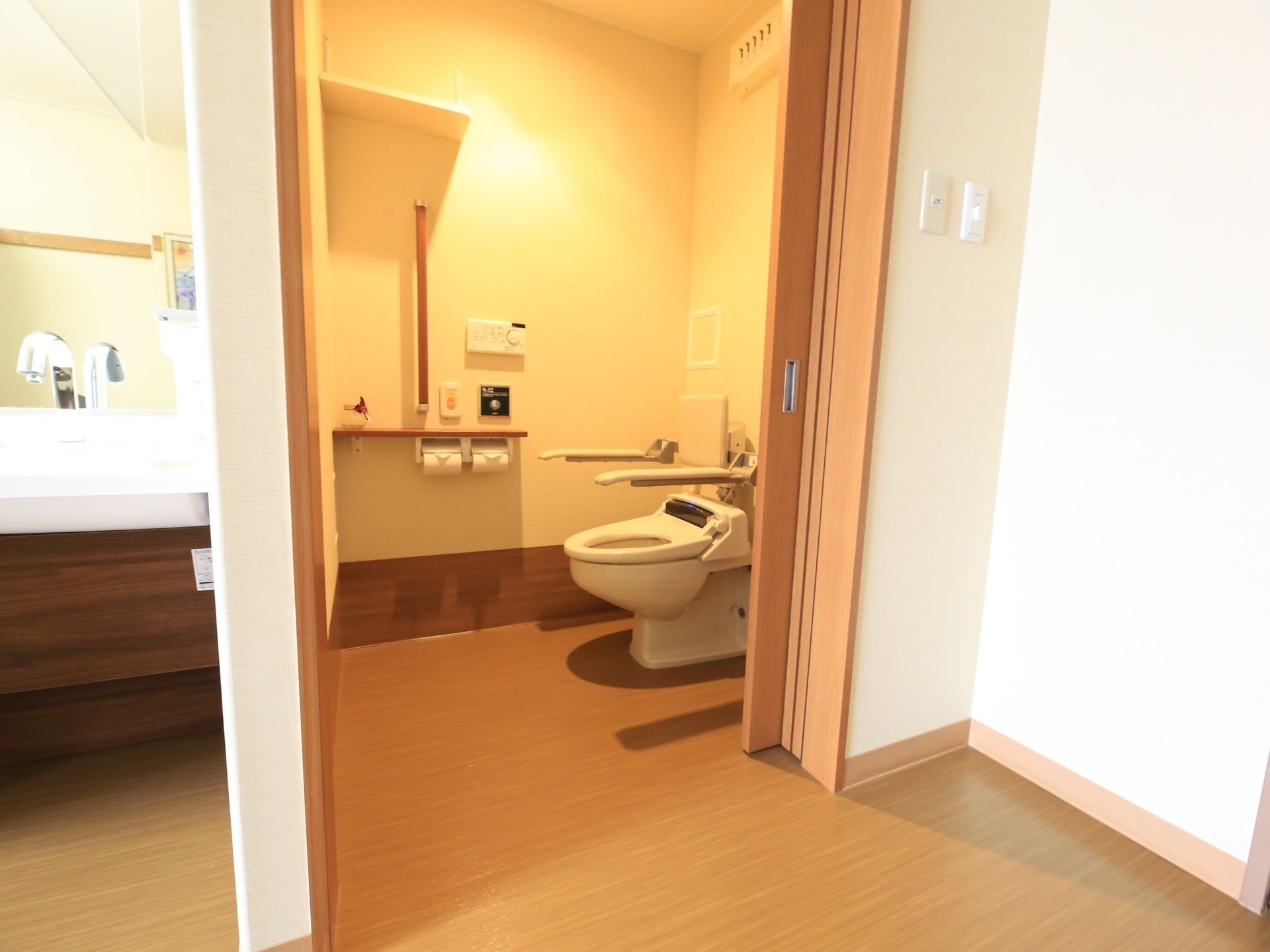 居室のトイレは、水タンクがついていないタイプの便器である。便座の周りに背もたれや可動式の手すりが設置されている。