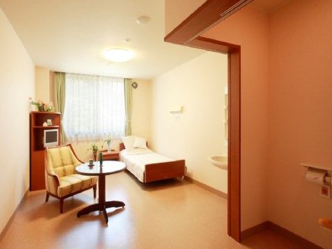 フローリングの床で、部屋やトイレの間に段差はない。ベッド、テレビなどが備え付けられている。大きな窓があり、明るい室内。