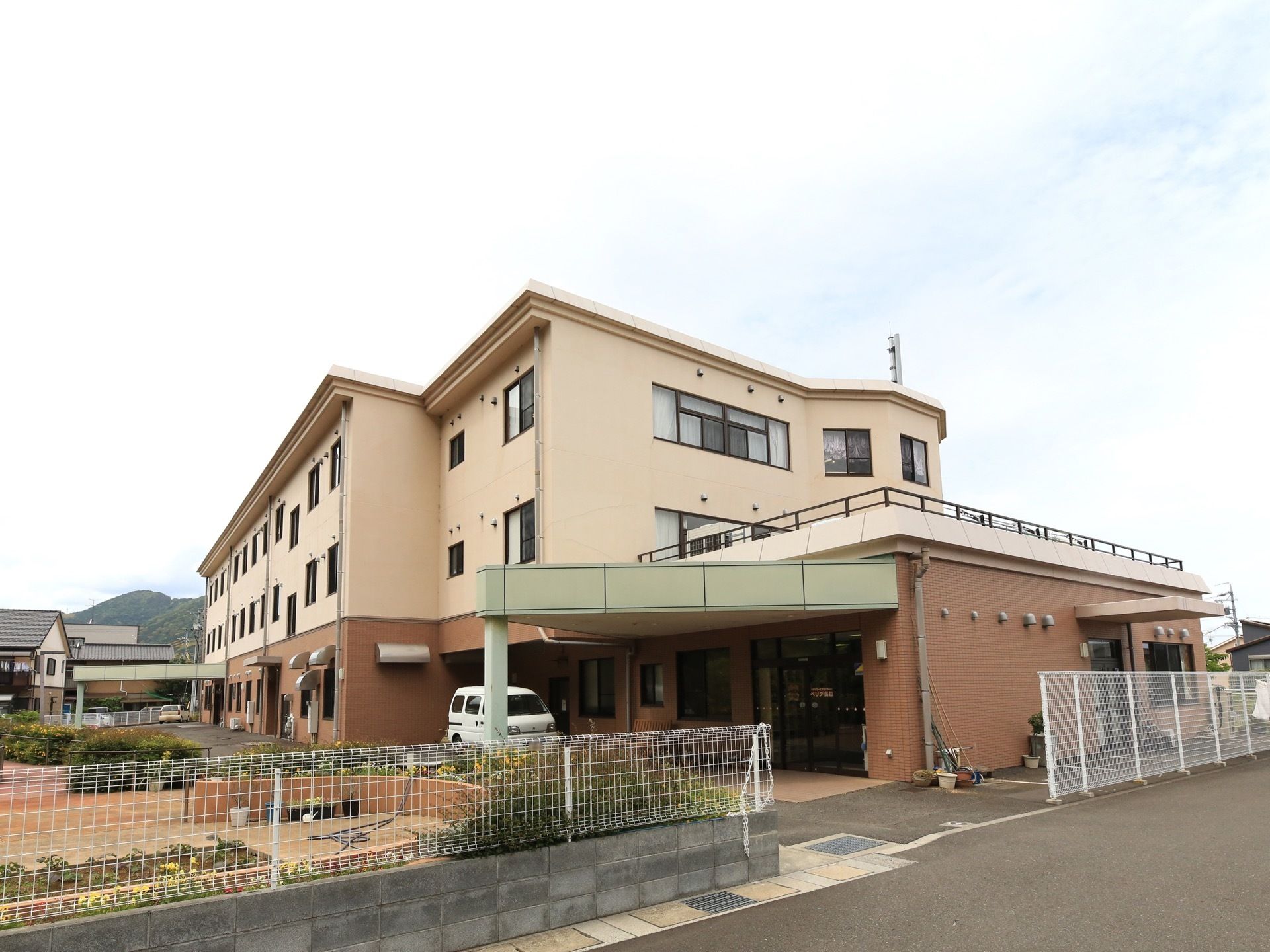 玄関が２か所にあり、どちらにも、三角形のひさしが設置されている。手前の玄関のすぐ近くに、白いバンが停まっている。