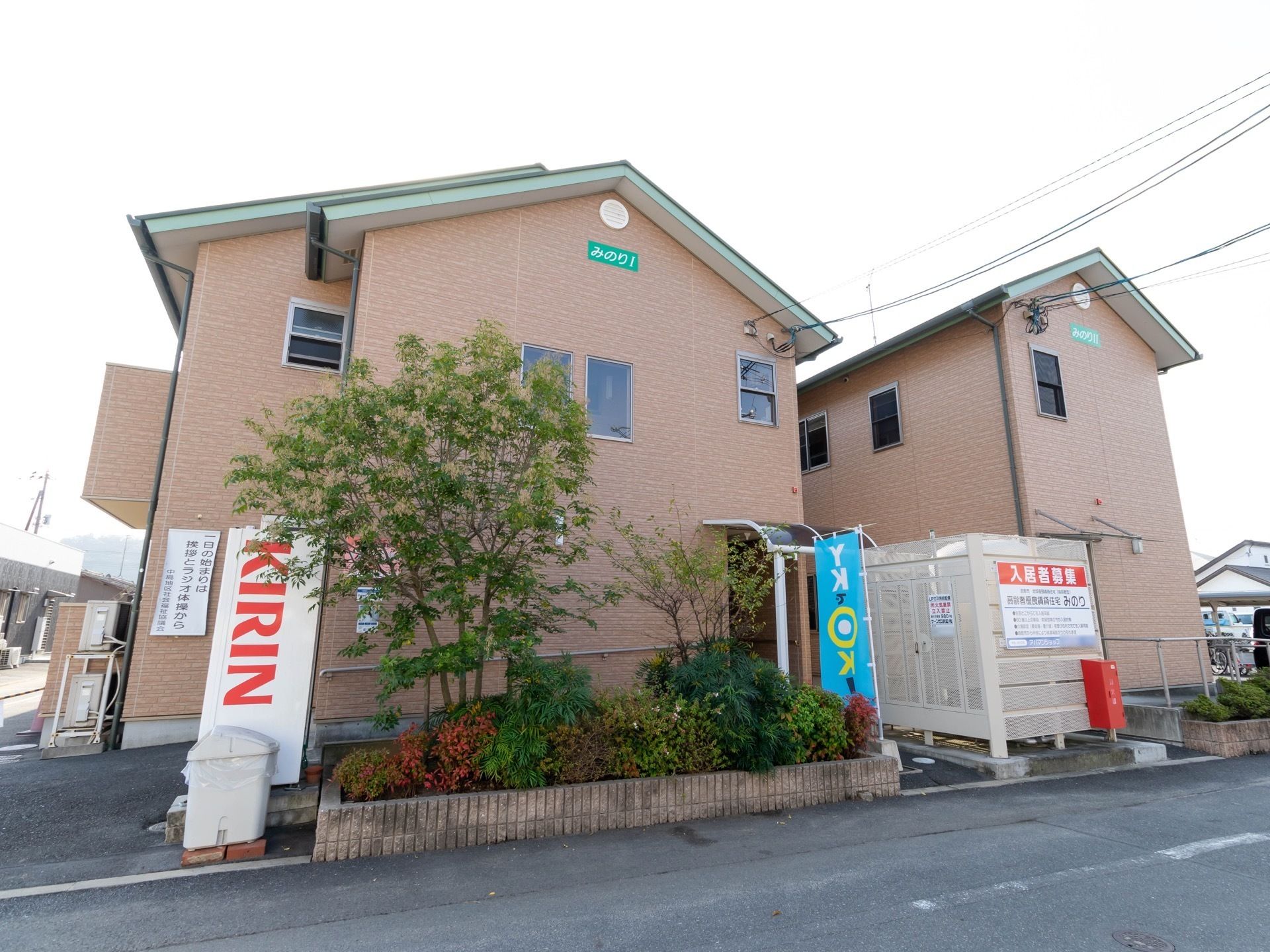 ２階建ての建造物で、温かみのあるピンクベージュである。自動販売機が置かれている。日当たり良好である。