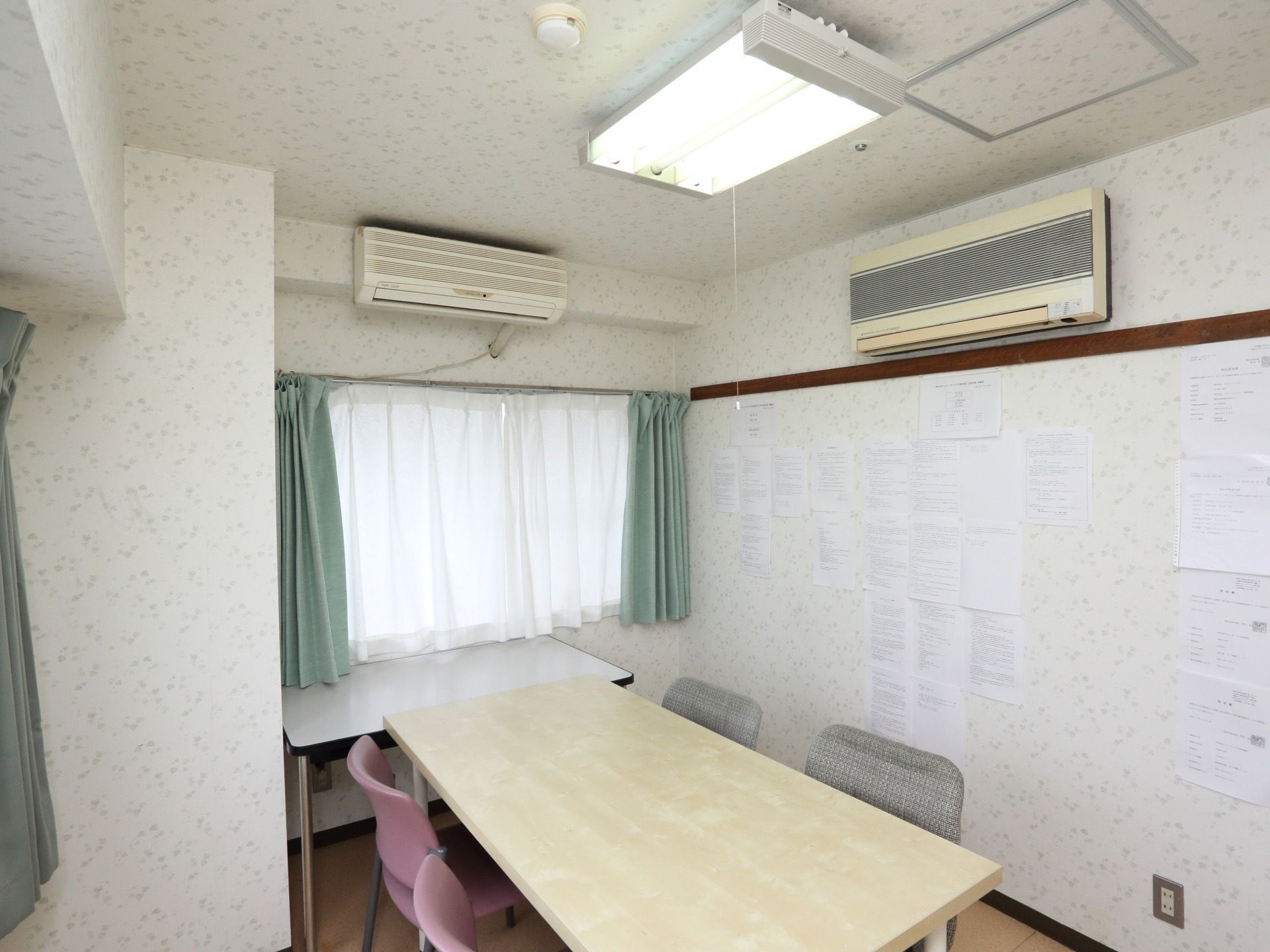 机と４脚の椅子が置かれている。壁には模様入りの壁紙が使われており、数多くの張り紙がされている。エアコンを完備している。