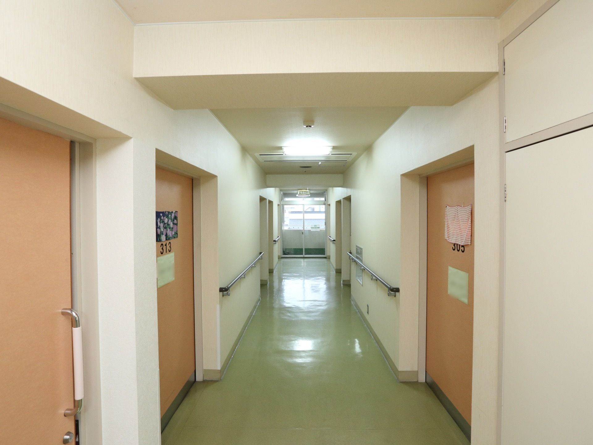 壁が白く明るい廊下である。通路幅が広く、居室の入り口はスライドドアになっている。両側に手すりが設置されている。