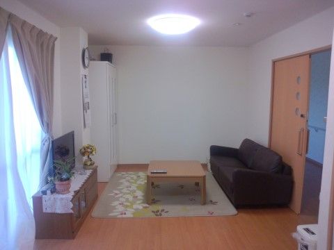 室内に大きめの茶色のソファーがあり、のんびりと過ごすことができる。白色の壁とベージュ色のフローリングが清潔感がある。