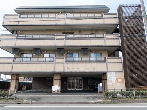施設の外観で、敷地に入る前にアコーディオン式のゲートが取り付けてある。入り口前に、黒板、柱に掲示物が貼ってある。玄関わきに自販機がある。