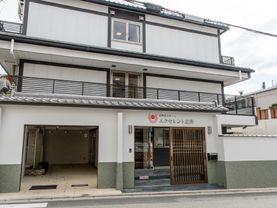 鉄骨造り3階建ての施設の外観で、引き戸の玄関である。黒いフェンスがついている。郵便受けが設置してある。