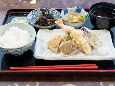食事の一例で、お盆の上に盛り付けてある。ごはん、てんぷら、吸い物、香の物のほかに小鉢がついている。赤い箸が1膳置いてある。
